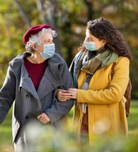 Caregiver assiste anziana durante una passeggiata al parco tenendolo per il braccio