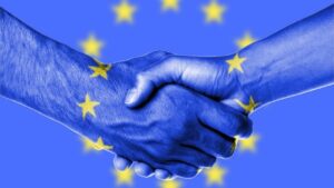 La commissione europea, due mani si stringono avendo come sfondo la bandiera dell'europa