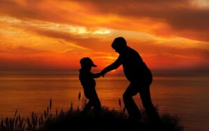 immagine in contro-luce di due persone che si tengono per mano al tramonto