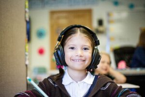 Copertina di Educazione e tecnologie digitali al tempo del Covid. Un ossimoro o un’opportunità? - una bambina con le cuffie sovraurali ride in camera e si prepara ad una lezione