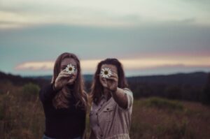 Due ragazze si abbracciano e mostrano due fiori appena raccolti dal campo dove si trovano al tramonto - Copertina di Contro ogni forma di violenza di genere e su minori, il bando del programma europeo CERV