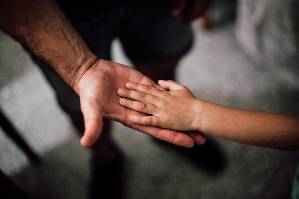 La mano di un adulto e di un bambino appoggiate una sull'altra. Immagine di copertina di un articolo di Secondo Welfare in cui si parla del Decreto Lavoro e delle novità che prevede in tema di fringe benefit di welfare aziendale