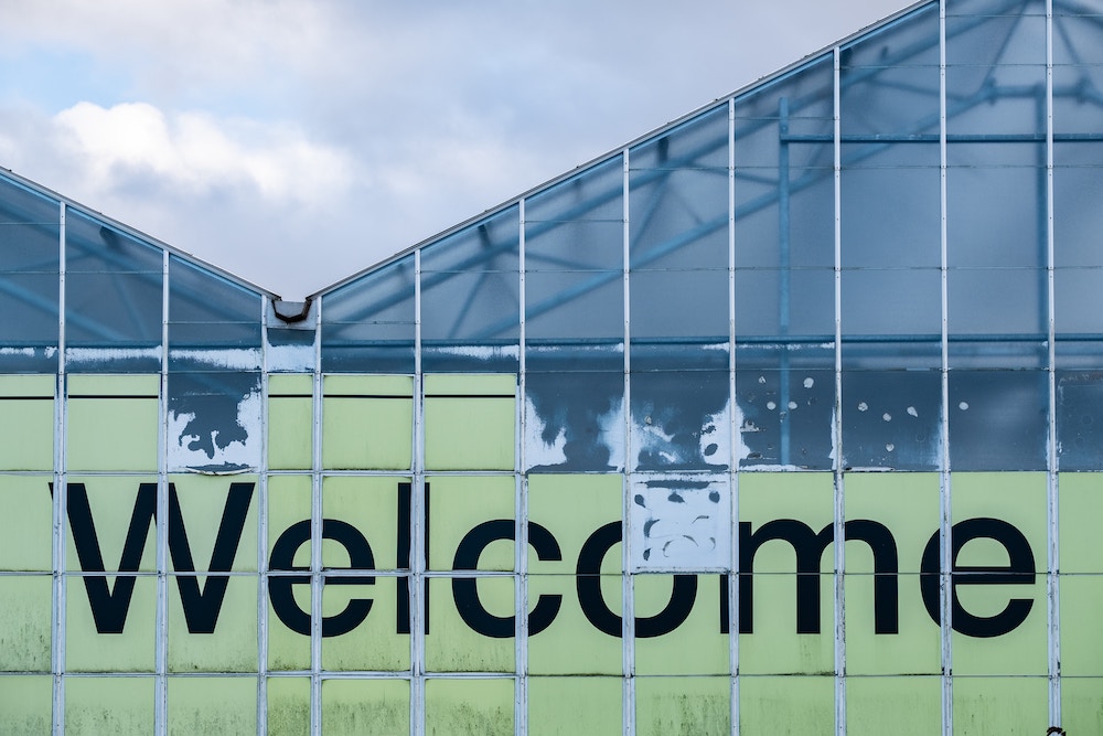 Un muro con scritto "welcome" rovinato. Immagine di copertina di un articolo di Secondo Welfare che propone una recensione del libro "Rifugiati e solidali" di Maurizio Ambrosini