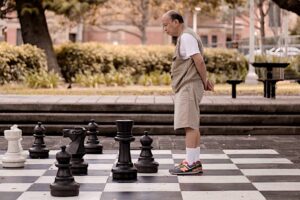 Un uomo anziano su una scacchiera gigante. Immagine di copertina di un articolo che spiega la differenza tra white economy e silver economy.