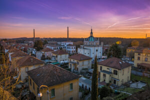 Crespi d'Adda al tramonto. Immagine di copertina di un articolo di Secondo Welfare sul libro "Al di qua del fiume"