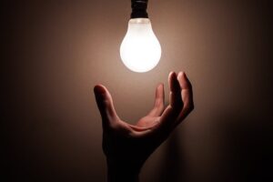 Una mano cerca di raggiungere una lampadina. Immagine di copertina di un articolo sul tema "Welfare Energetico Locale: per nuove politiche pubbliche contro la povertà energetica (e non solo)"