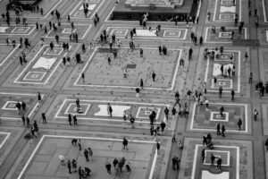 Una foto in bianco e nero di persone che camminano a Milano. Immagine di copertina di un articolo di Secondo Welfare sull'atlante di genere di Milano.