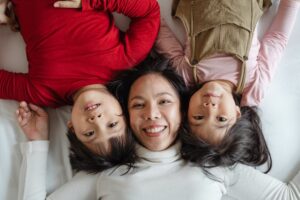 Foto di una mamma con figli sdraiati sul letto. Immagine di copertina di un articolo di Secondo Welfare sull'impatto diretto o indiretto che le politiche pubbliche possono avere sulle relazioni familiari e sullo strumento FamILens.