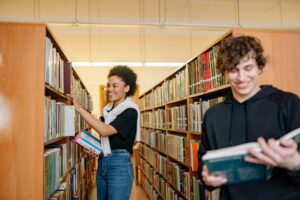 Ragazzo e ragazza in biblioteca con libri in mano. Foto utilizzata come immagine di copertina di un articolo di Percorsi di secondo welfare su come creare biblioteche a misura di giovani.