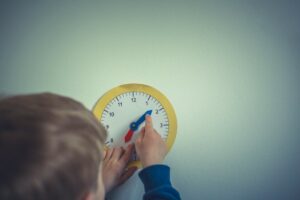 bambino che sposta le lancette di un orologio di carta. Immagine di copertina di un articolo di Percorsi di secondo welfare su ombre e luci dell’applicazione di quella parte della riforma della “Buona Scuola” che riguarda il potenziamento dell'educazione prescolare, 10 anni dopo.