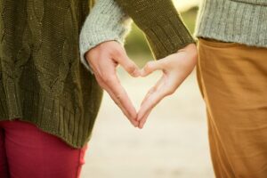 persone che formano un cuore con le loro mani. Immagine di copertina di un articolo di Percorsi di secondo welfare sul concetto di famiglia.