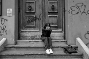 ragazza triste seduta sui gradini. Immagine di copertina di un articolo di Percorsi di secondo welfare sulla povertà alimentare.