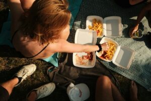 gruppo di adolescenti che mangiano seduti sul prato. immagine di copertina di un articoli di Percorsi di secondo welfare sulla povertà alimentare tra gli adolescenti.