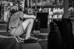 foto in bianco e nero di un ragazzo seduto per terra. Immagine di copertina di un articolo di Percorsi di secondo welfare sulla salute mentale dei giovani.