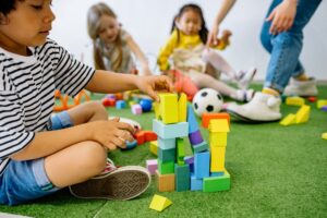 Bambini che giocano per terra. Immagine di copertina di un articolo di Percorsi di secondo welfare sul festival di nidi fioriti, due giornate per chi si prende cura dell'infaniza