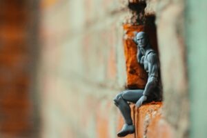 Un omino di plastica su un muro di mattoni. Immagine di copertina di un articolo di secondo welfare sull'Assegno di inclusione e sulle nuove domande di sussidio per oltre mezzo milione di persone.