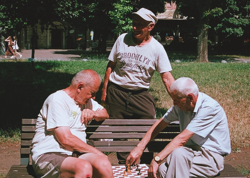 Anziani giocano a scacchi su una panchina in un parco. Immagine di copertina di un articolo sulla strategia del Comune di Bergamo per la longevità, scritto sulla rivista Nessi dall'Assessora Marcella Messina