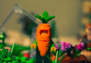 Un lego vestito da carota. Immagine di copertina dell'articolo di Percorsi di Secondo Welfare Coltivare un orto o comprare le verdure al mercato? Strategie per usare l’intelligenza artificiale nella programmazione sociale?"