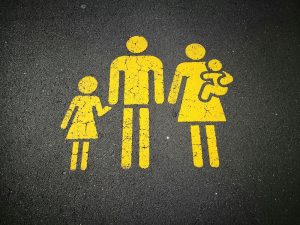 Famiglia stilizzata usata per segnaletica stradale orizzontale. Immagine di copertina di un articolo di Percorsi di Secondo Welfare sulle nuove previsioni di welfare aziendale per i familiari beneficiari dei benefit e i premi di risultato
