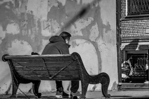 Foto in bianco e nero di un uomo seduto su una panchina. Immagine di copertina di un articolo di Percorsi di Secondo Welfare sulla povertà
