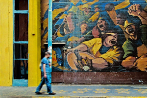 uomo che cammina davanti a un murales. Immagine di copertina di un articolo di Percorsi di Secondo Welfare su Il welfare al contrario: quando, invece di proteggere, discrimina ed esclude