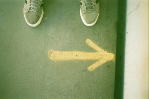 Piedi di un ragazzo davanti a una freccia gialla su sfondo verde. Immagine di copertina di un articolo sul libro Investire nel futuro: asset building e disuguaglianze educative