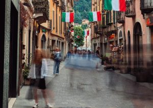 Una via in Italia con persone in movimento e bandiere. Immagine di copertina di un articolo di Percorsi di secondo welfare su Comuni e welfare locale