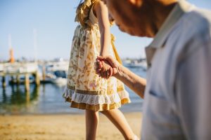 nonno che tiene la mano della nipote sulla spiaggia in una giornata di sole. Immagine di copertina di un articolo di Percorsi di Secondo Welfare su invecchiamento e patto intergenerazionale